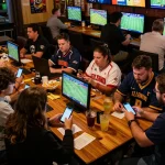 Sky88live patrons cheering for their teams while placing bets on mobile devices in a lively sports bar